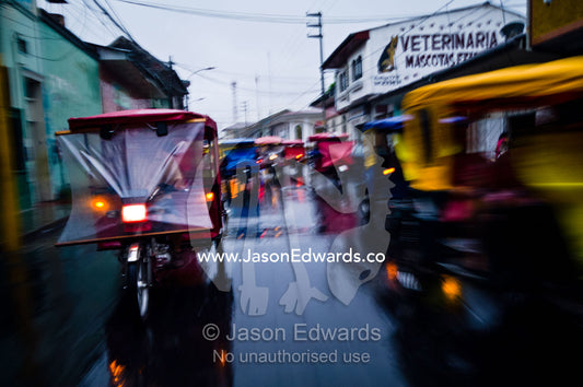 Traffic headlights swirl past an auto rickshaw on a rainy night in an Amazon River town. Iquitos, Amazon Basin, Loreto Region, Maynas Province, Peru.
