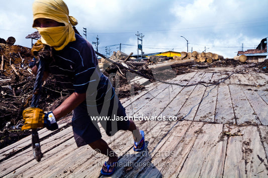 A logging mill laborer tows a heavy steel cable to a barge to collect cut rainforest tree logs. Puerto Masusa, Iquitos, Amazon Basin, Loreto Region, Maynas Province, Peru.