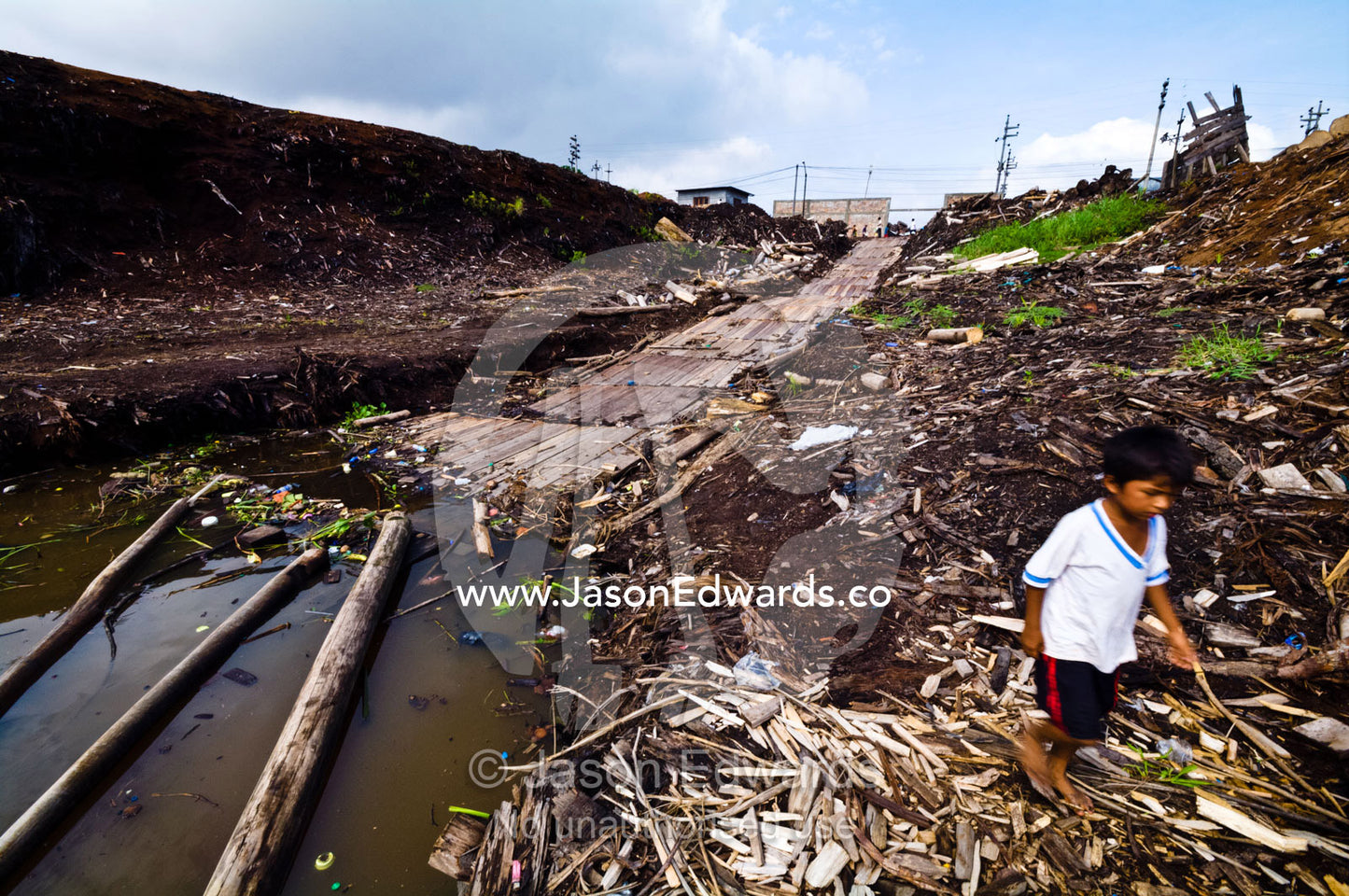 A boy walks through the pollution on the Amazon River shore near a logging mill. Puerto Masusa, Iquitos, Amazon River, Rio Amazonas, Amazon Basin, Loreto Region, Maynas Province, Peru.