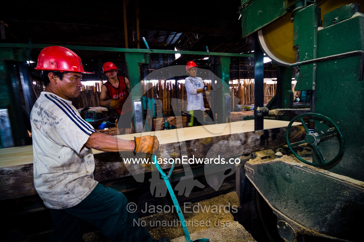 A laborer operates a band saw to cut the bark from an Amazon rainforest tree in a logging mill. Puerto Masusa, Iquitos, Amazon Basin, Loreto Region, Maynas Province, Peru.