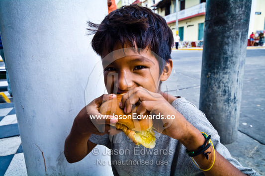 A boy enjoys eating a sandwich for lunch in an Amazon river town cafe. Plaza de Armas, Iquitos, Amazon Basin, Loreto Region, Maynas Province, Peru.