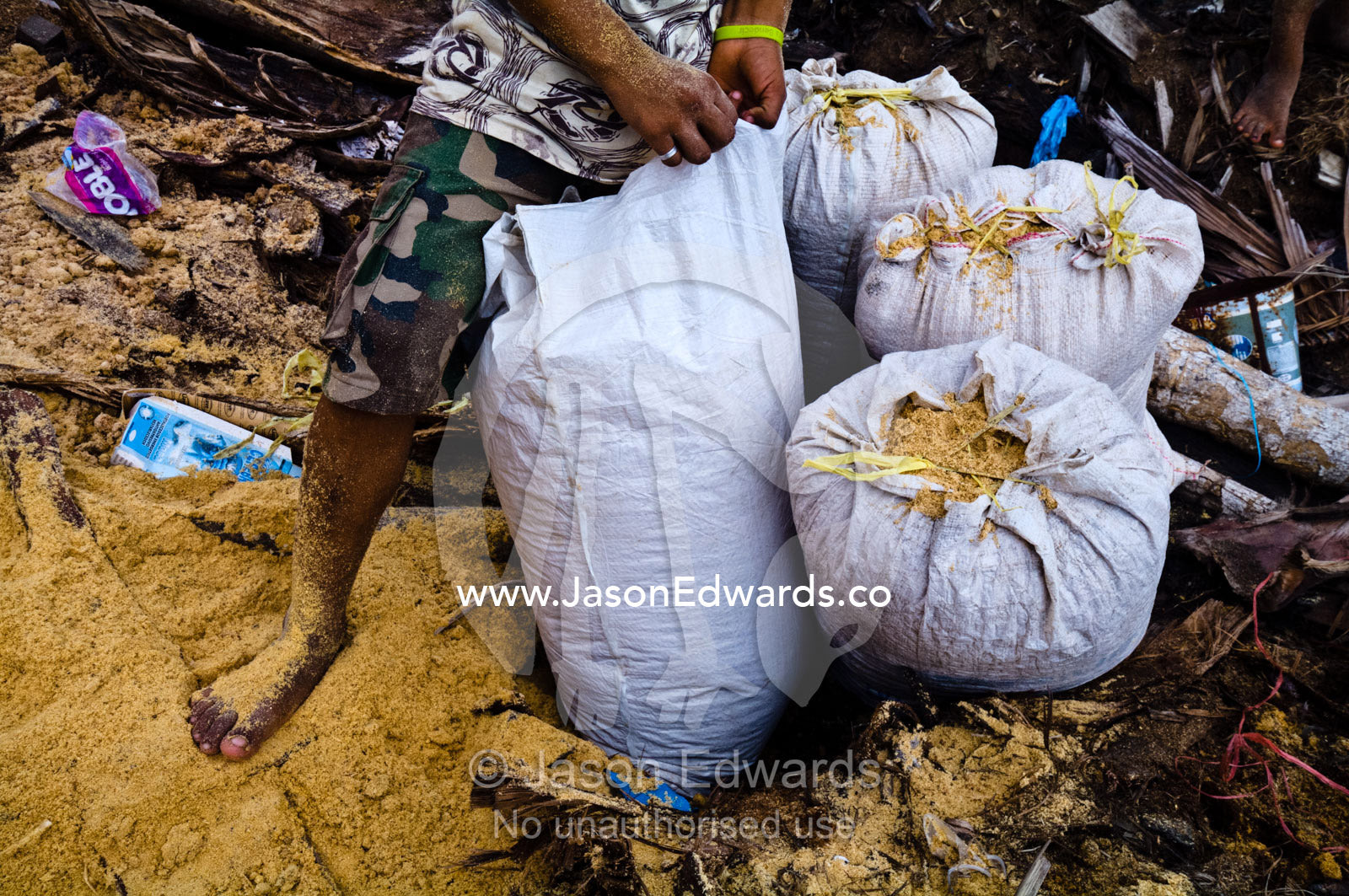 A boy collects sawdust waste in plastic bags to spread on the dirt floor of his family home. Puerto Masusa, Iquitos, Amazon Basin, Loreto Region, Maynas Province, Peru.