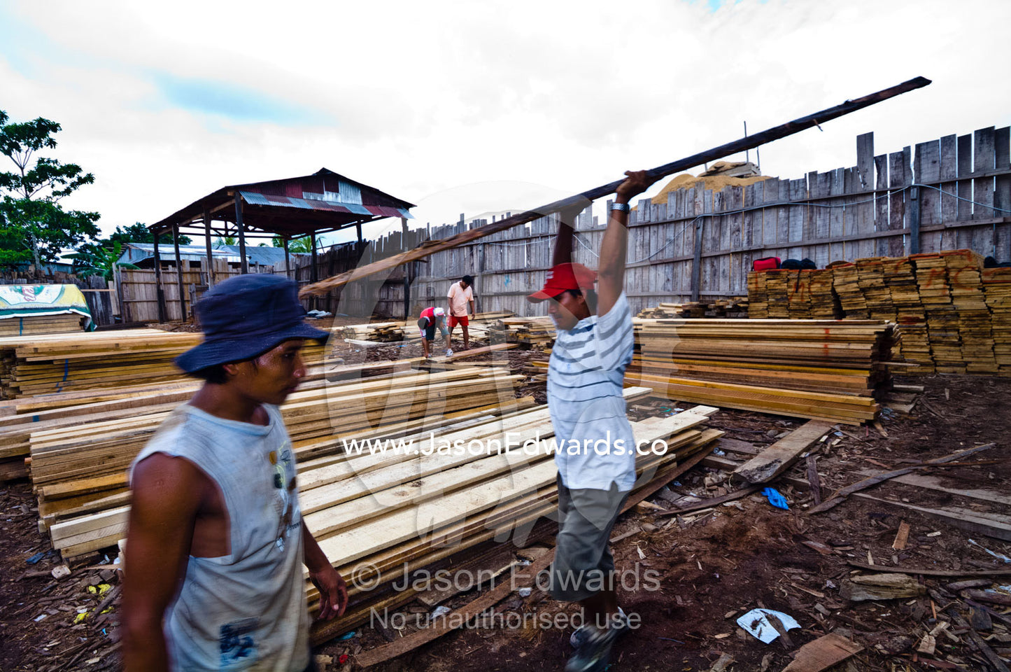Laborers carry timber planks sold to clients in a logging mill yard. Puerto Masusa, Iquitos, Amazon Basin, Loreto Region, Maynas Province, Peru.
