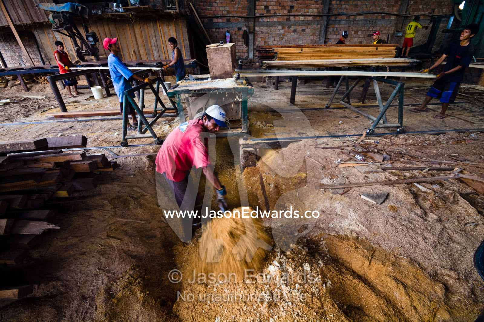 A laborer in a logging mill shovels sawdust from underneath a jigsaw blade. Puerto Masusa, Iquitos, Amazon Basin, Loreto Region, Maynas Province, Peru.