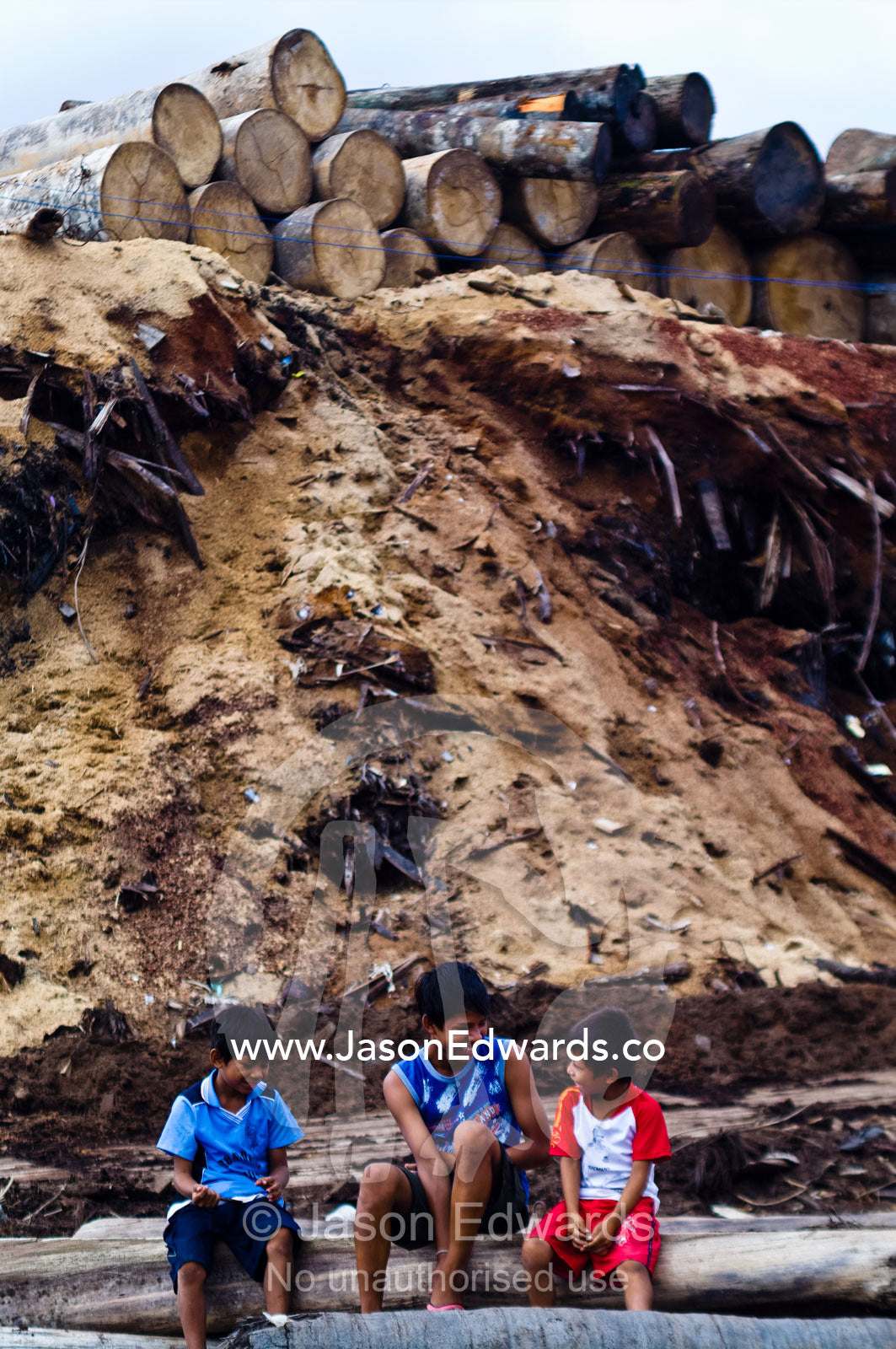 Boys from an Amazon river town resting amongst logs and sawdust mounds at a logging mill. Puerto Masusa, Iquitos, Amazon Basin, Loreto Region, Maynas Province, Peru.