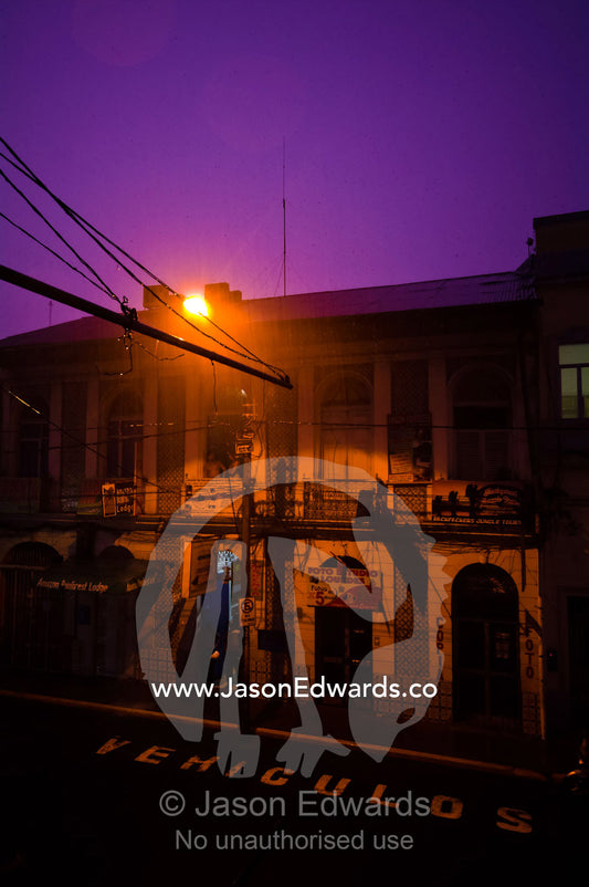 From doorways and balconies people watch flash lightning turn the night sky turn purple during a thunderstorm. Iquitos, Amazon Basin, Loreto Region, Maynas Province, Peru.