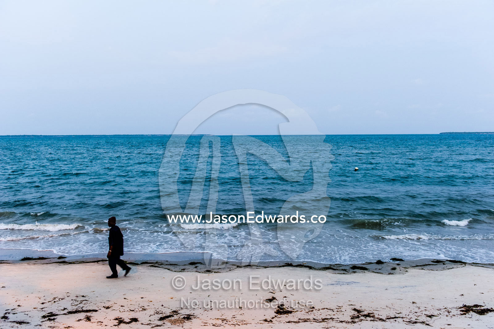 A man walking along an empty beach after finishing work at sunset. Dar es Salaam, Kawe, Tanzania, Africa.
