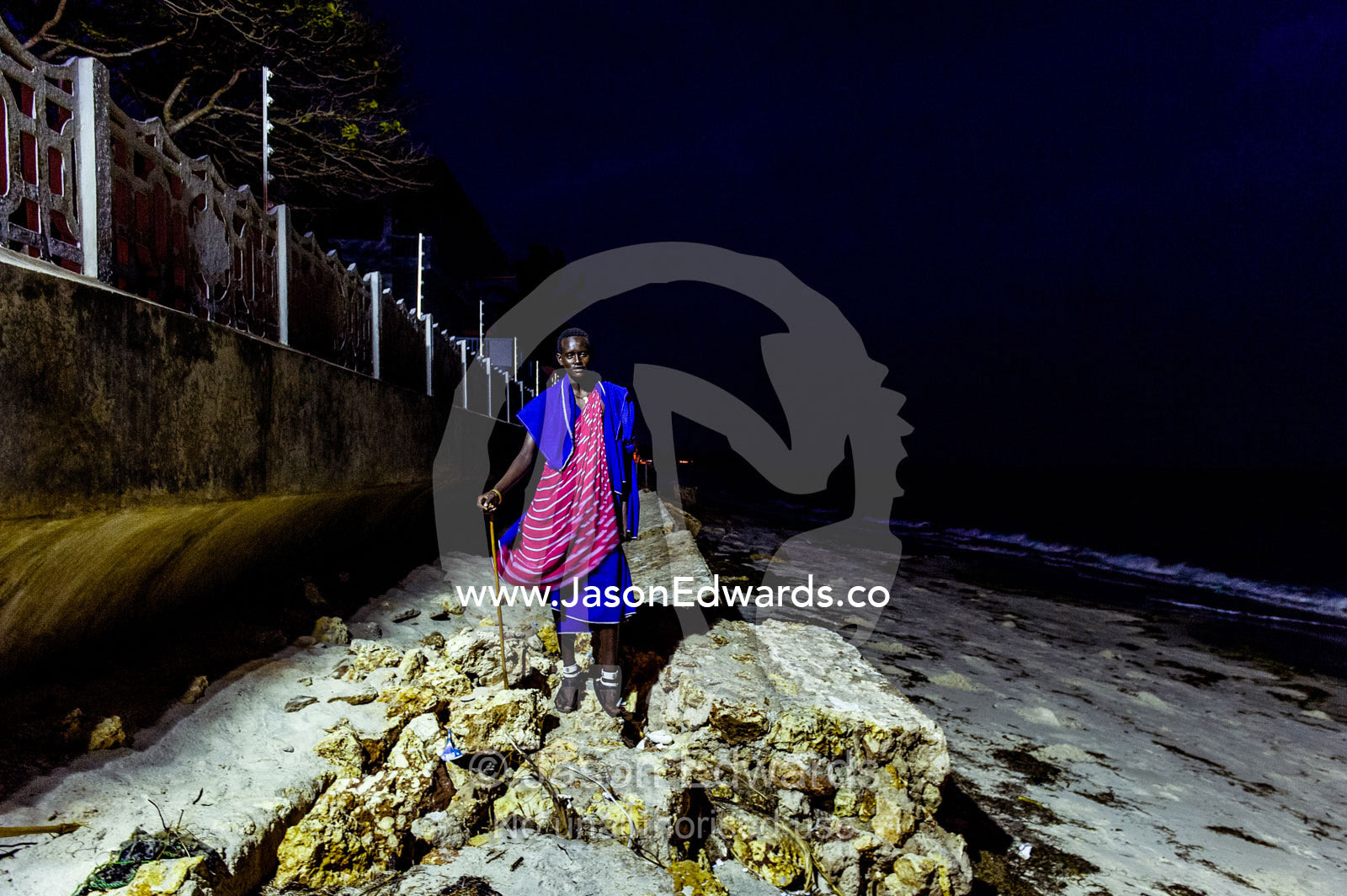 A young Masai warrior lured to the city waits to entertain guests at a seaside hotel. Dar es Salaam, Kawe, Tanzania, Africa.