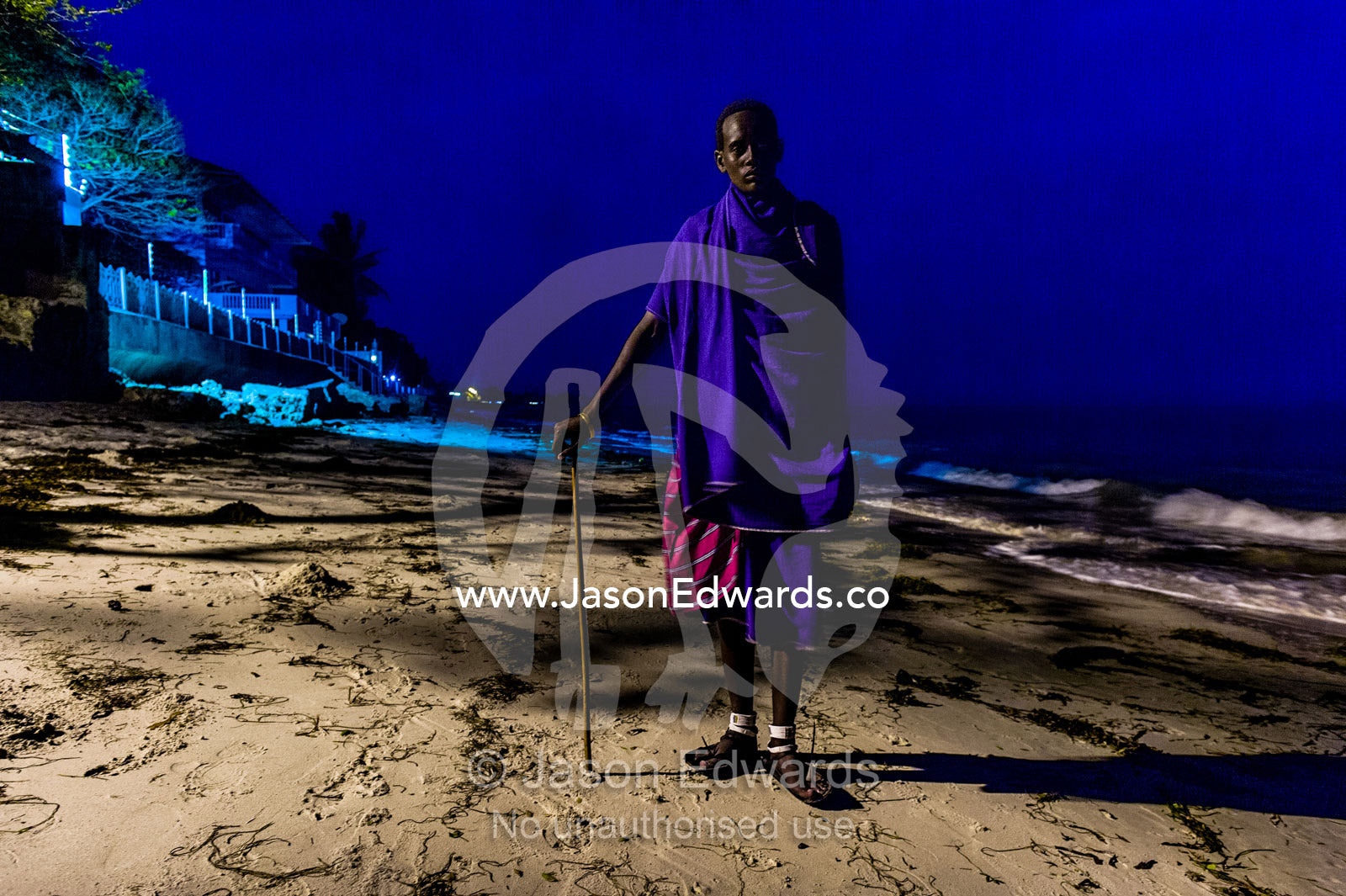 A young Masai warrior lured to the city waits to entertain guests at a seaside hotel. Dar es Salaam, Kawe, Tanzania, Africa.