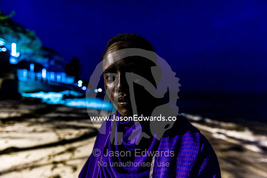 A young Masai warrior lured to the city waits to entertain guests at a seaside hotel. Dar es Salaam, Kawe, Tanzania, Africa.