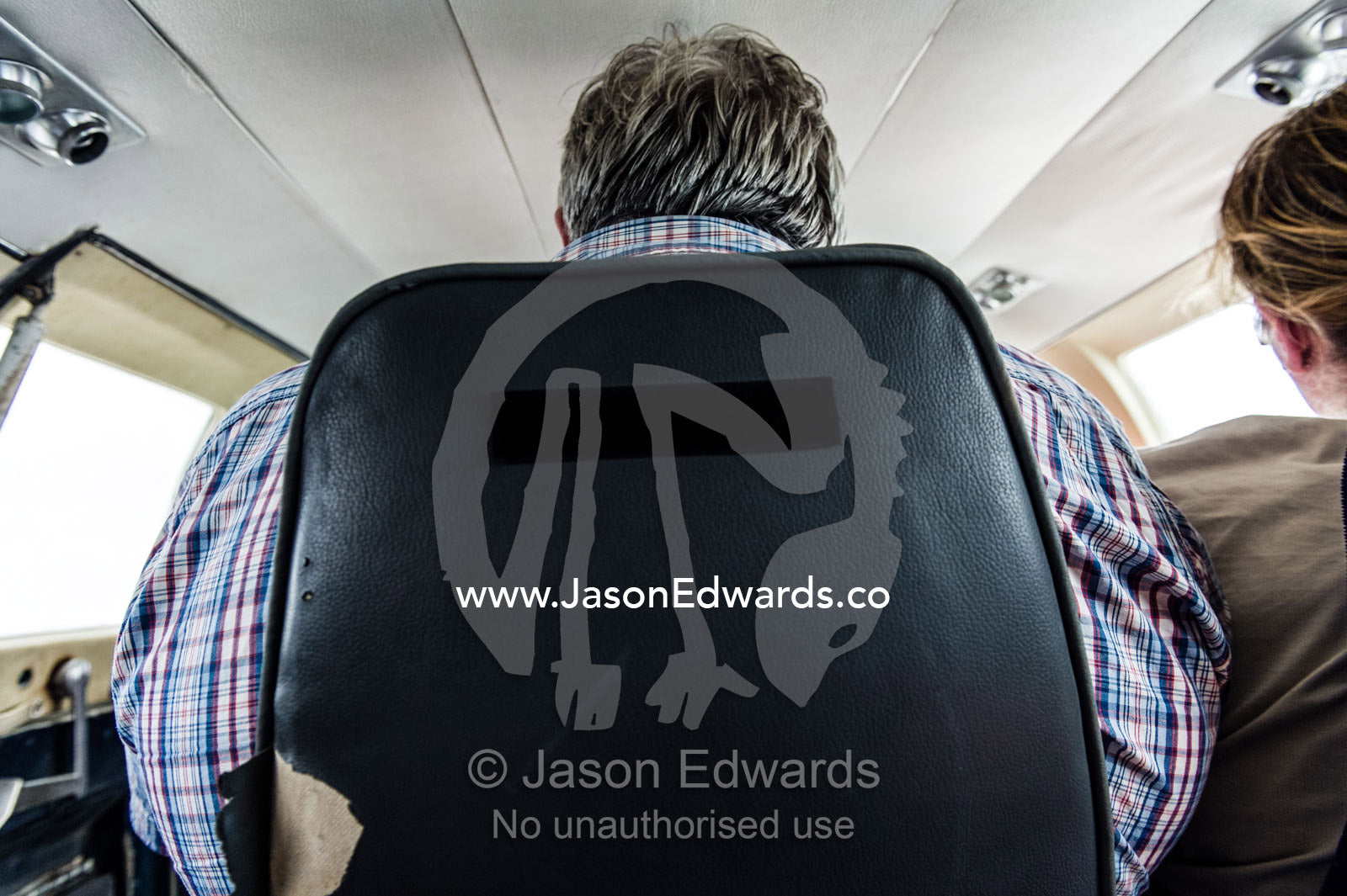 A large man seated in the rear seat of a light plane in flight over Africa. Arusha, Arusha Airport, Arusha Region, Tanzania.