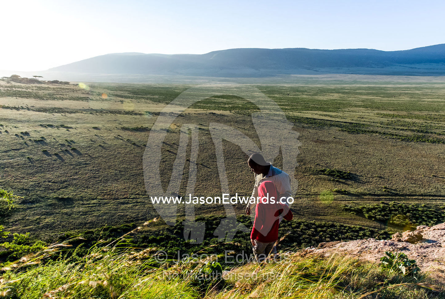 A safari guide assists a small child to climb down the steep surface of a rocky outcrop. Arusha, Nasera Rock, Angata Kiti Valley, Ngorongoro Conservation Area, Crater Highlands, Tanzania.
