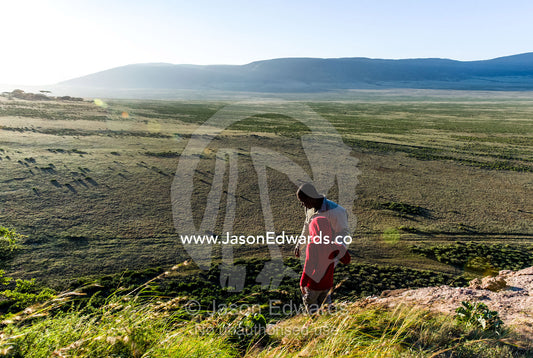 A safari guide assists a small child to climb down the steep surface of a rocky outcrop. Arusha, Nasera Rock, Angata Kiti Valley, Ngorongoro Conservation Area, Crater Highlands, Tanzania.