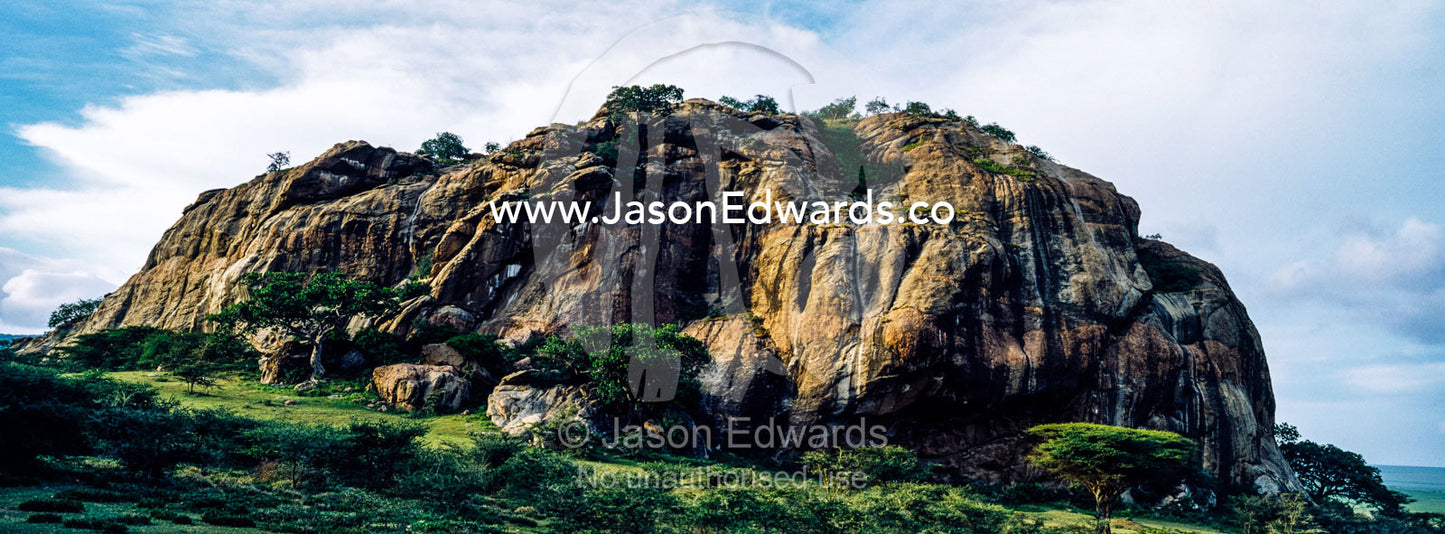 An enormous rocky outcrop rises from the savannah plain like a monolith. Arusha, Nasera Rock, Angata Kiti Valley, Ngorongoro Conservation Area, Crater Highlands, Tanzania.