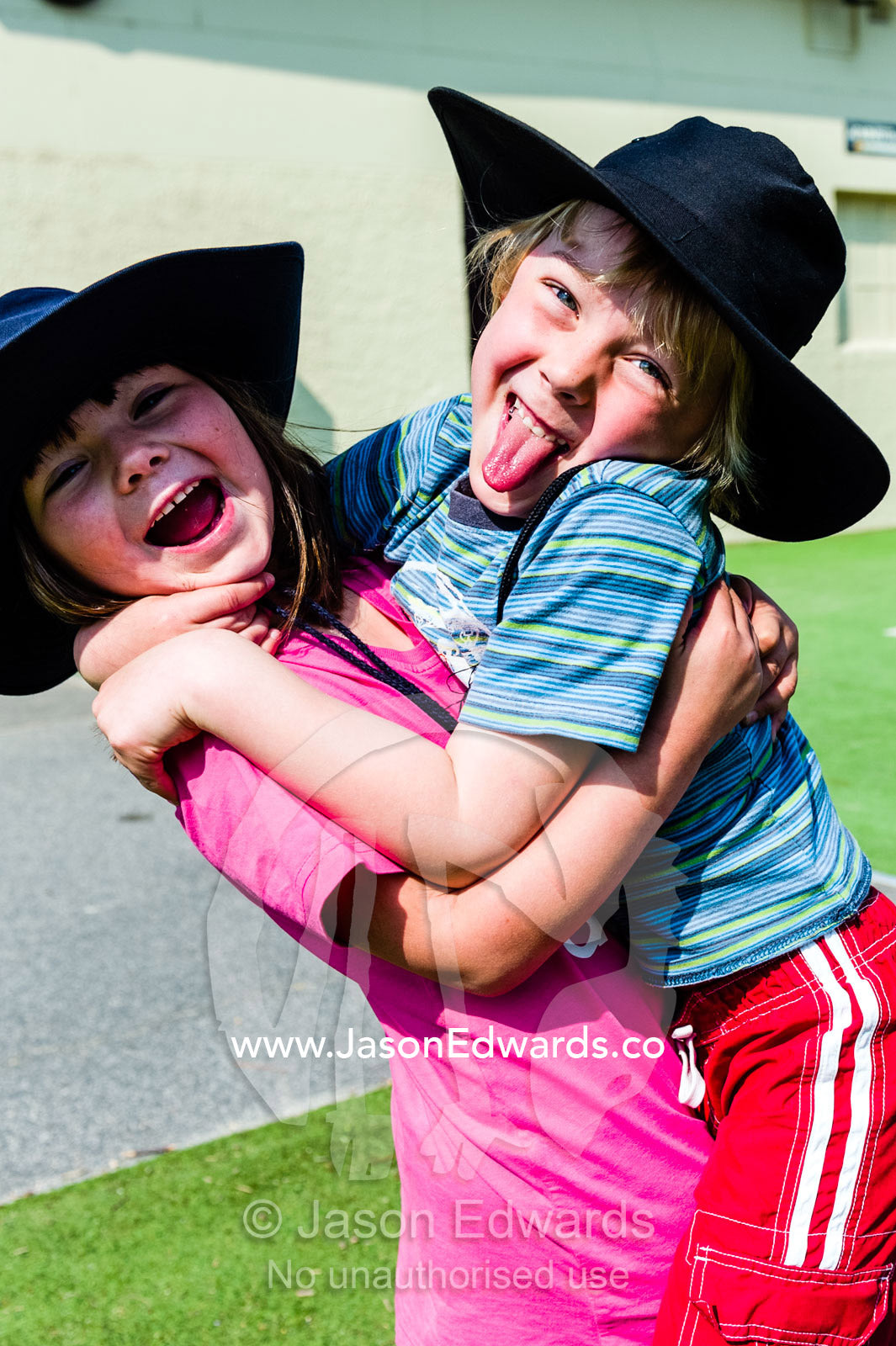 Two friends hug each other in the school play ground on a summers day. Carlton North Primary School, Carlton North, Melbourne, Victoria, Australia.