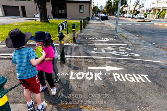 School children resting on a chain fence near a bicycle path crossing. Carlton North Primary School, Carlton North, Melbourne, Victoria, Australia.