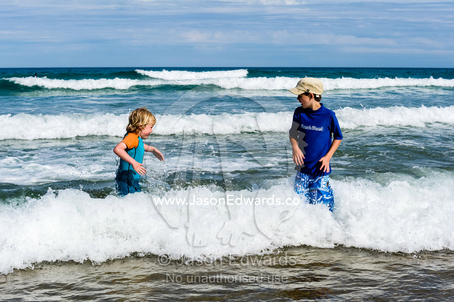 Two friends playing in the icy ocean waves on a sunny winters day. Wye River, Great Ocean Road, Victoria, Australia.