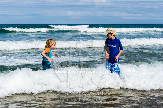 Two friends playing in the icy ocean waves on a sunny winters day. Wye River, Great Ocean Road, Victoria, Australia.