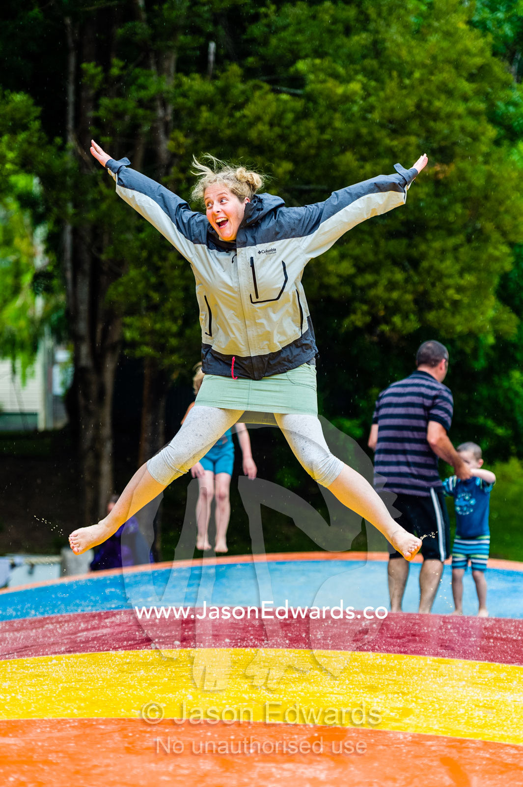 A woman clowning around doing star jumps on an inflatable cushion. Wye River, Great Ocean Road, Victoria, Australia.