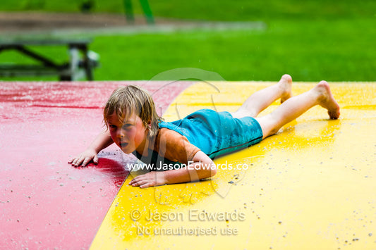 A boy injures himself jumping on an inflatable cushion in a wetsuit. Wye River, Great Ocean Road, Victoria, Australia.