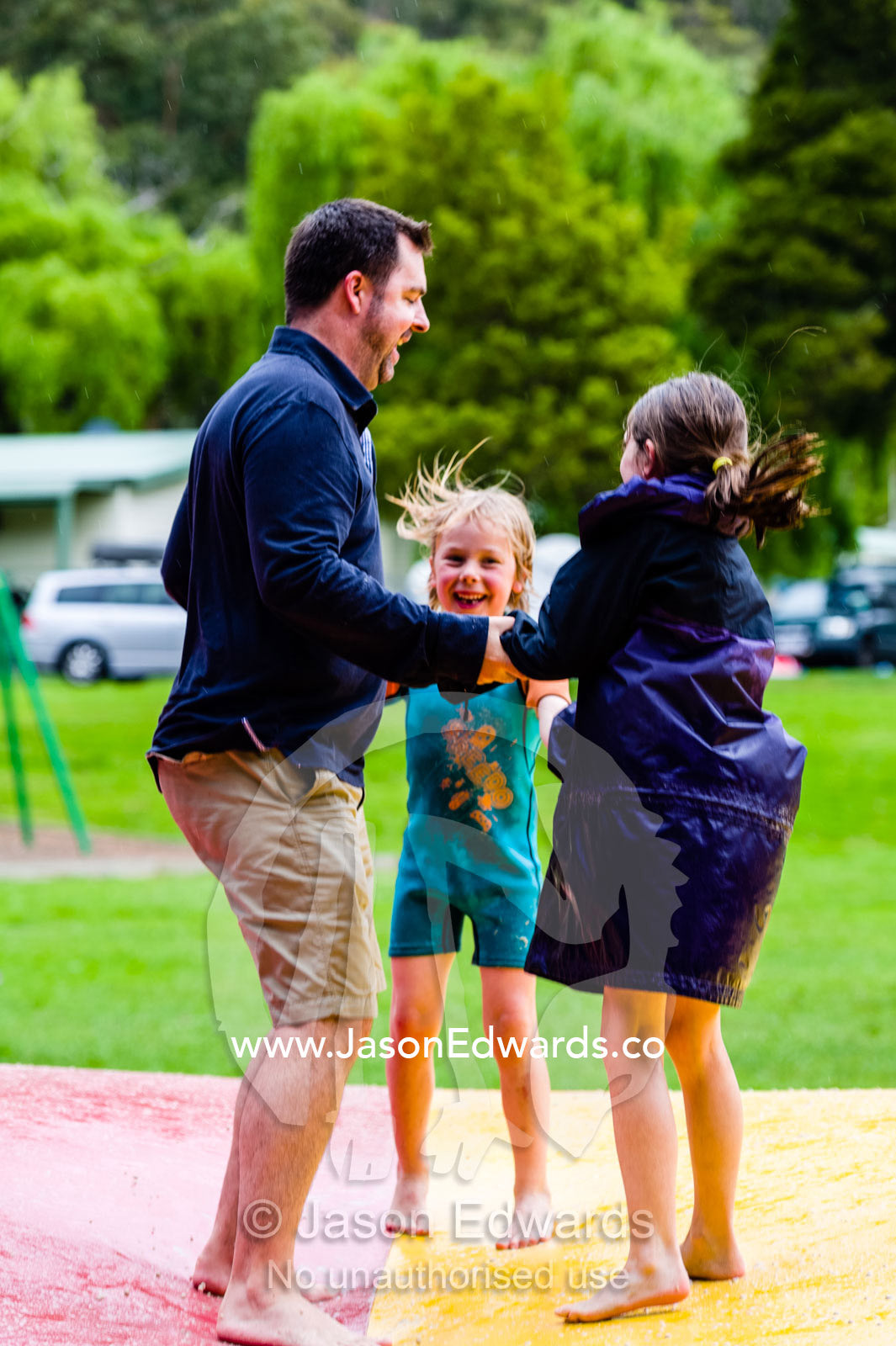 A man laughing and jumping with children on an inflatable cushion. Wye River, Great Ocean Road, Victoria, Australia.