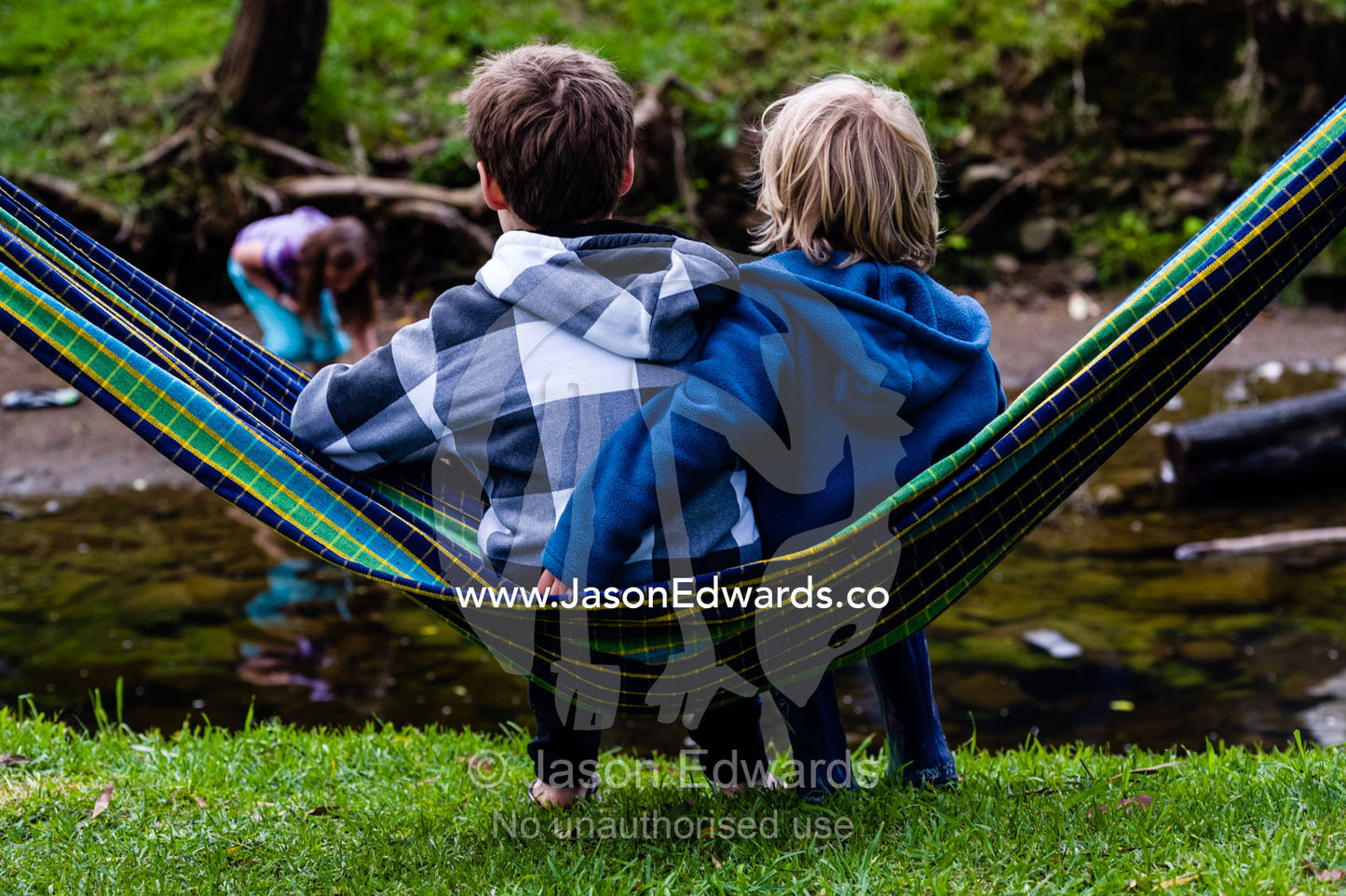 Two friends swing in a hammock beside a small stream in a campground. Wye River, Great Ocean Road, Victoria, Australia.