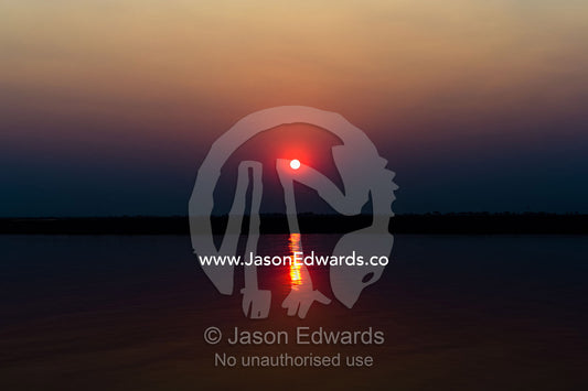 A flaming sunset over a still wetland during the burning season. Chobe River, Chobe National Park, Botswana.