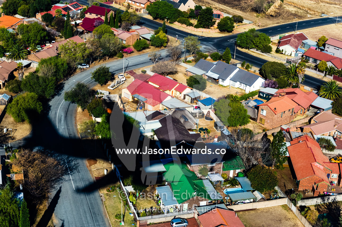 The shadow of a landing passenger jet shades houses in a suburb next to the airport. Johannesburg, Gauteng Province, South Africa, Africa.