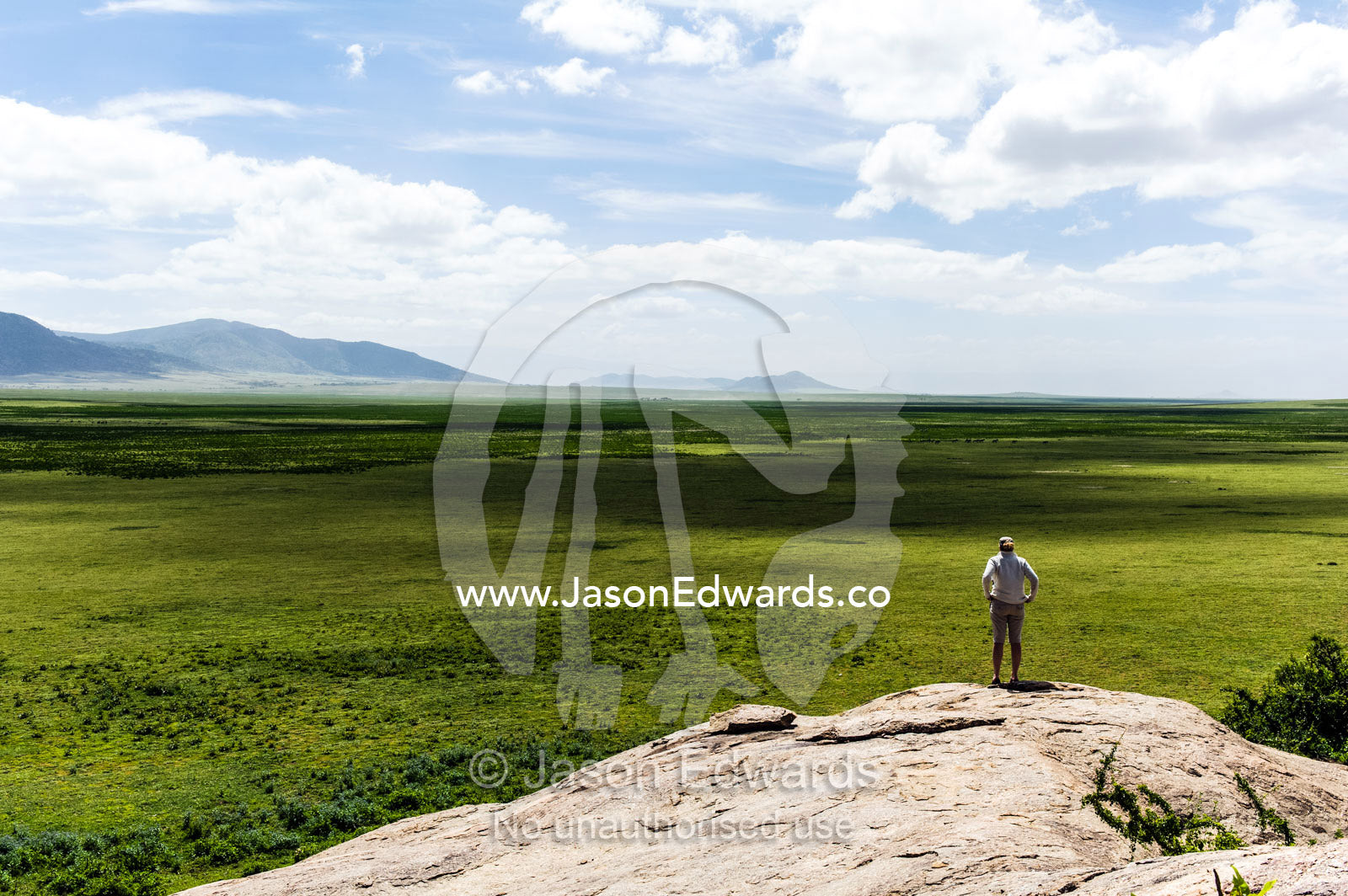 A tourist surveys the vast and endless African savannah from a granite kopje. Ngorongoro Conservation Area, Ngorongoro District, Tanzania.