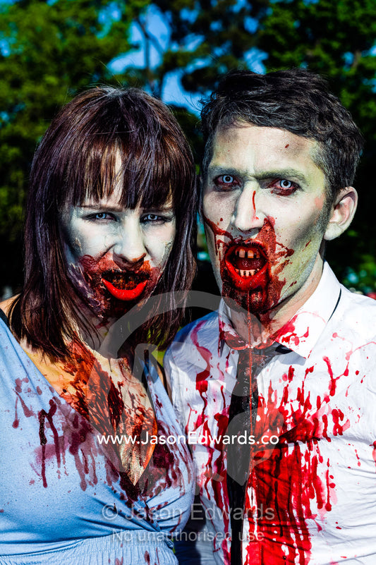 A snarling modern business couple dripping blood dressed as zombies. Queen Victoria Gardens, Royal Botanic Gardens, South Yarra, Melbourne, Victoria, Australia.