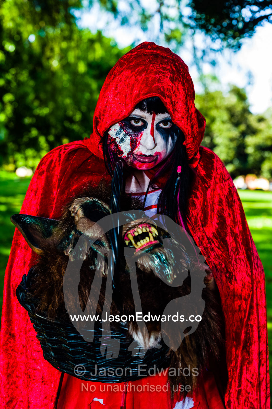 A zombie dressed as Little Red Riding Hood carries a wolf's head at a festival. Carlton Gardens, World Heritage Site, Carlton, Melbourne, Victoria, Australia.