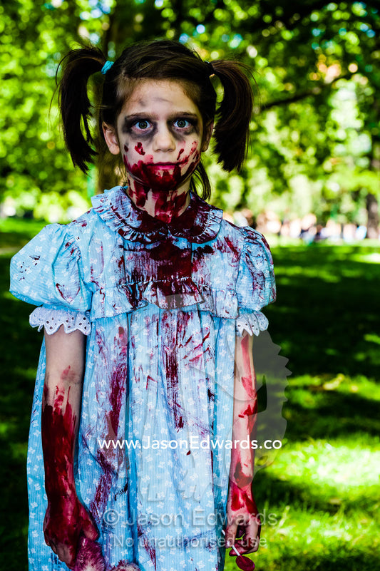 A blood-soaked zombie girl with pigtails in a pretty blue dress at a festival. Carlton Gardens, World Heritage Site, Carlton, Melbourne, Victoria, Australia.