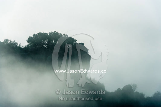 In a cold pre-dawn mist and fog surround a rocky granite outcrop known as a kopje. Moru Kopjes, Serengeti National Park, Serengeti, World Heritage Site, Tanzania.