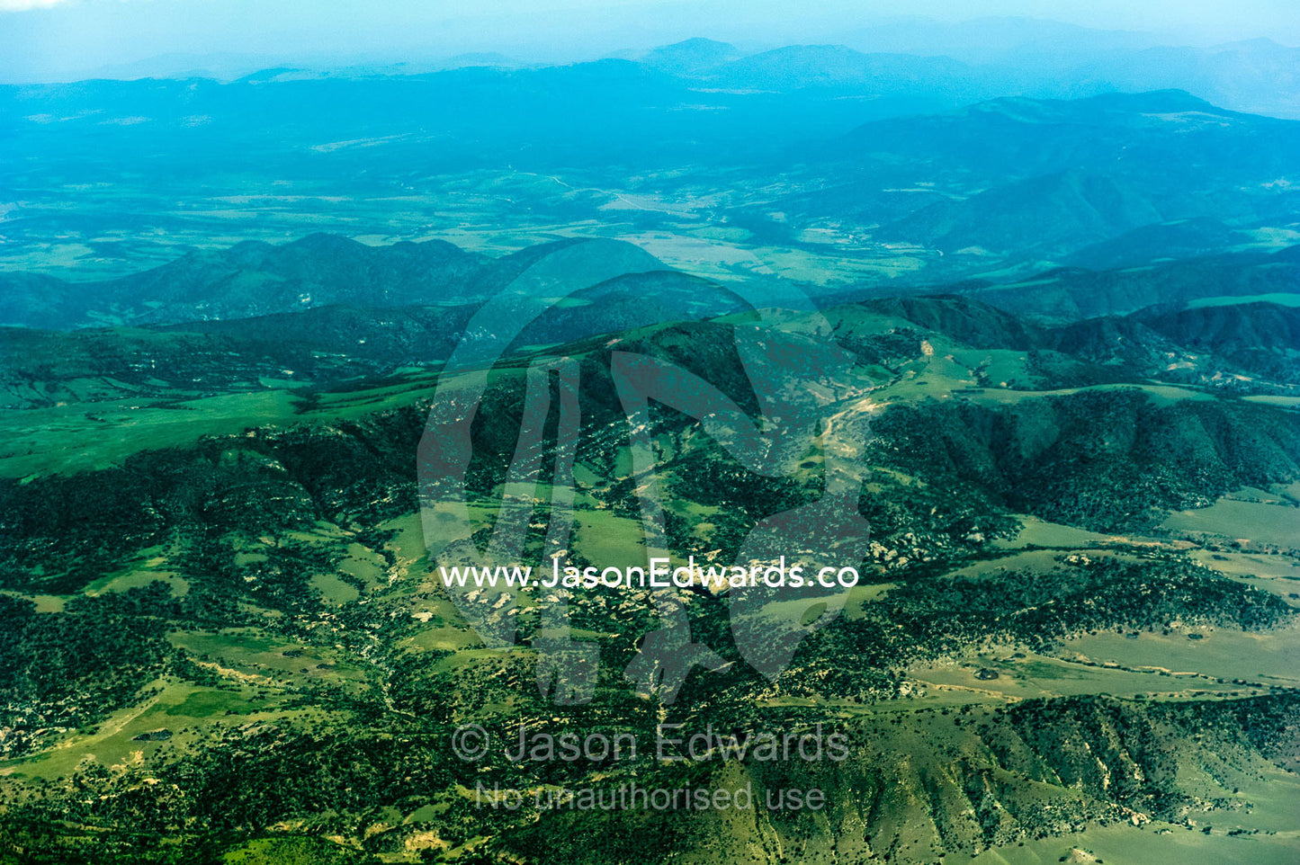 Forested volcanic mountain slopes and farms rise above the vast, green savannah plain. Crater Highlands, Ngorongoro Highlands, Serengeti National Park, Serengeti, Tanzania.