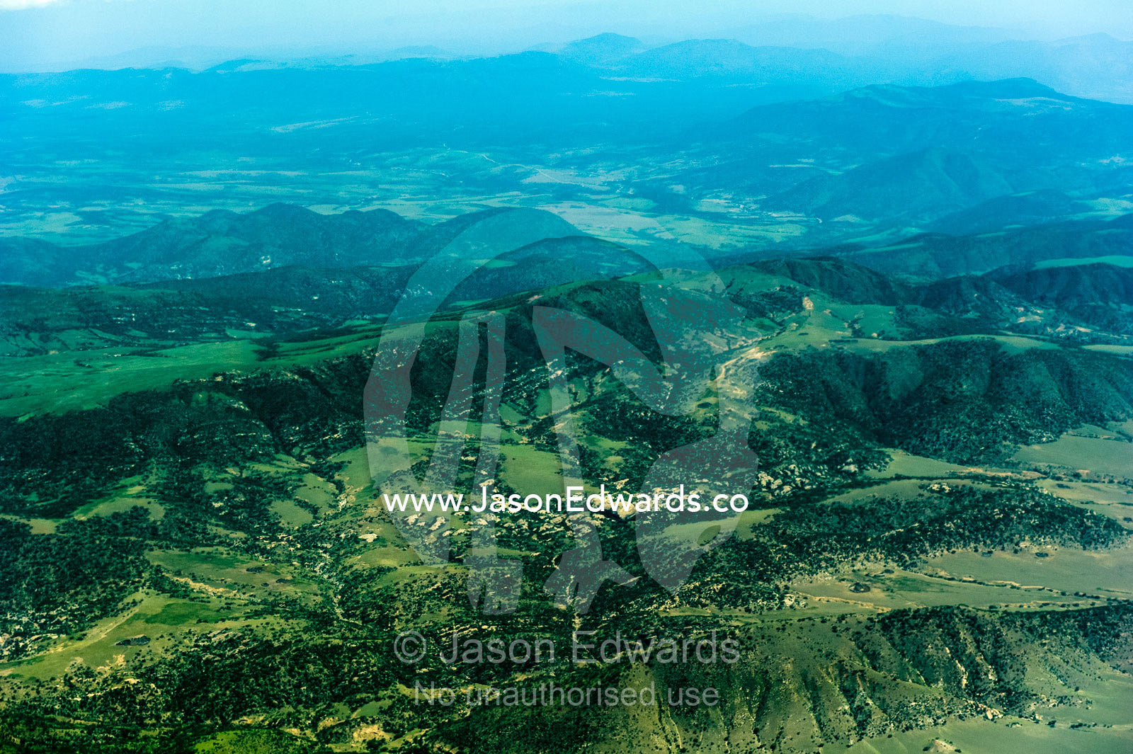 Forested volcanic mountain slopes and farms rise above the vast, green savannah plain. Crater Highlands, Ngorongoro Highlands, Serengeti National Park, Serengeti, Tanzania.