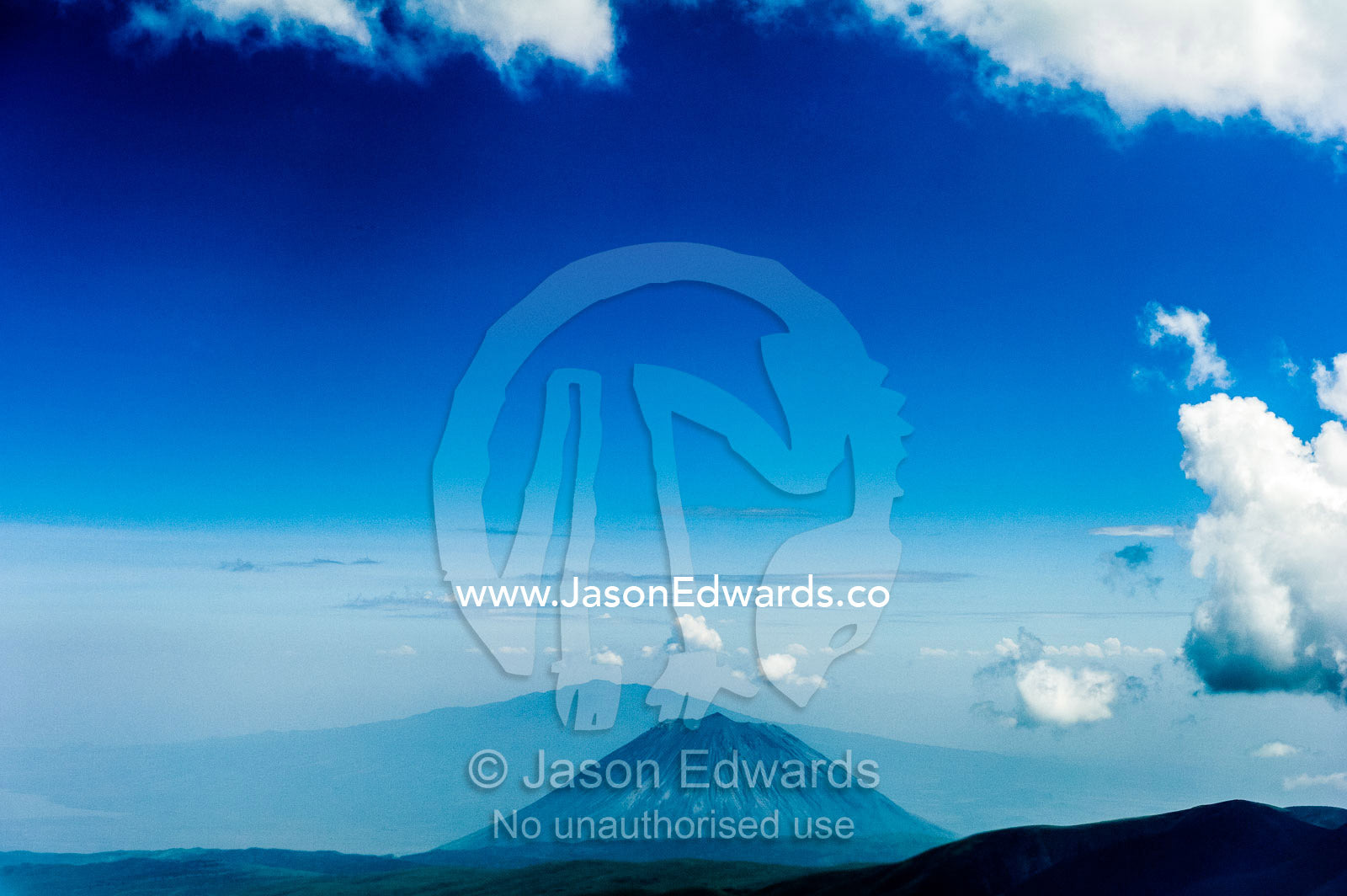 Clouds circle the summit of primeval volcano caldera shrouded in forests above the savannah plain. Crater Highlands, Ngorongoro Highlands, Serengeti National Park, Serengeti, Tanzania.