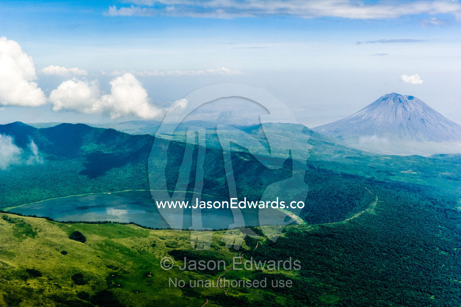 Clouds circle the summit of primeval volcano caldera shrouded in forests above the savannah plain. Crater Highlands, Ngorongoro Highlands, Serengeti National Park, Serengeti, Tanzania.
