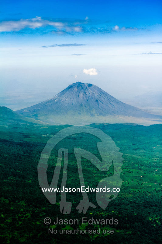 Clouds circle the summit of primeval volcano caldera shrouded in forests above the savannah plain. Crater Highlands, Ngorongoro Highlands, Serengeti National Park, Serengeti, Tanzania.