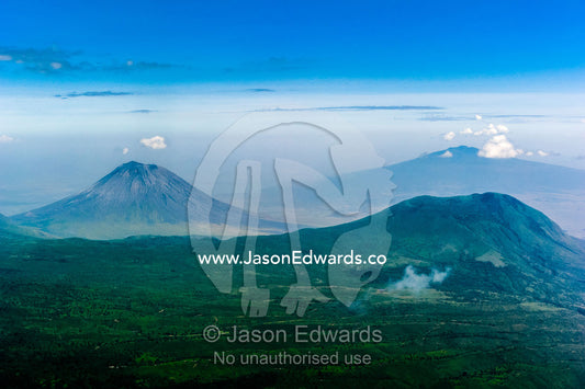 Clouds circle the summit of primeval volcano caldera shrouded in forests above the savannah plain. Crater Highlands, Ngorongoro Highlands, Serengeti National Park, Serengeti, Tanzania.