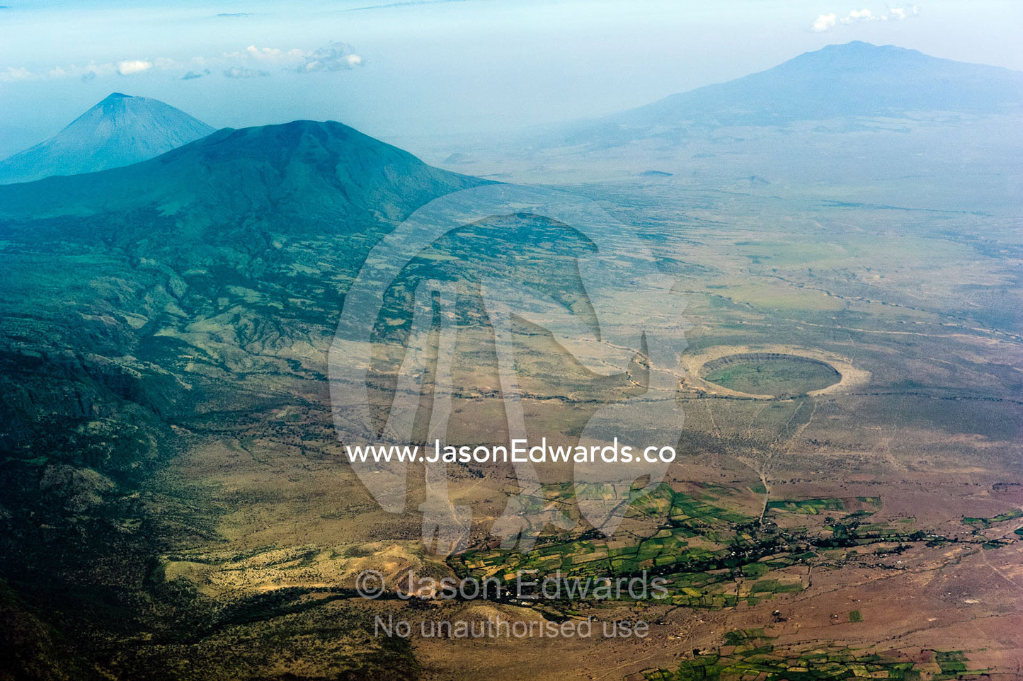 Clouds circle primeval volcano caldera shrouded in forests and an eroded caldera on the dry savannah plain. Crater Highlands, Ngorongoro Highlands, Serengeti National Park, Serengeti, Tanzania.