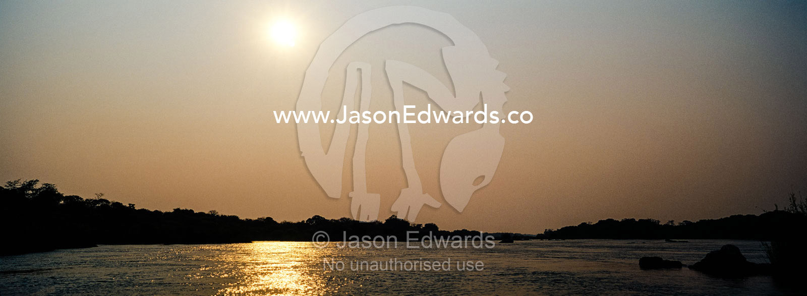 Dawn rises over a wide river flowing between riverbanks covered in forest. Chobe River, Chobe National Park, Botswana.