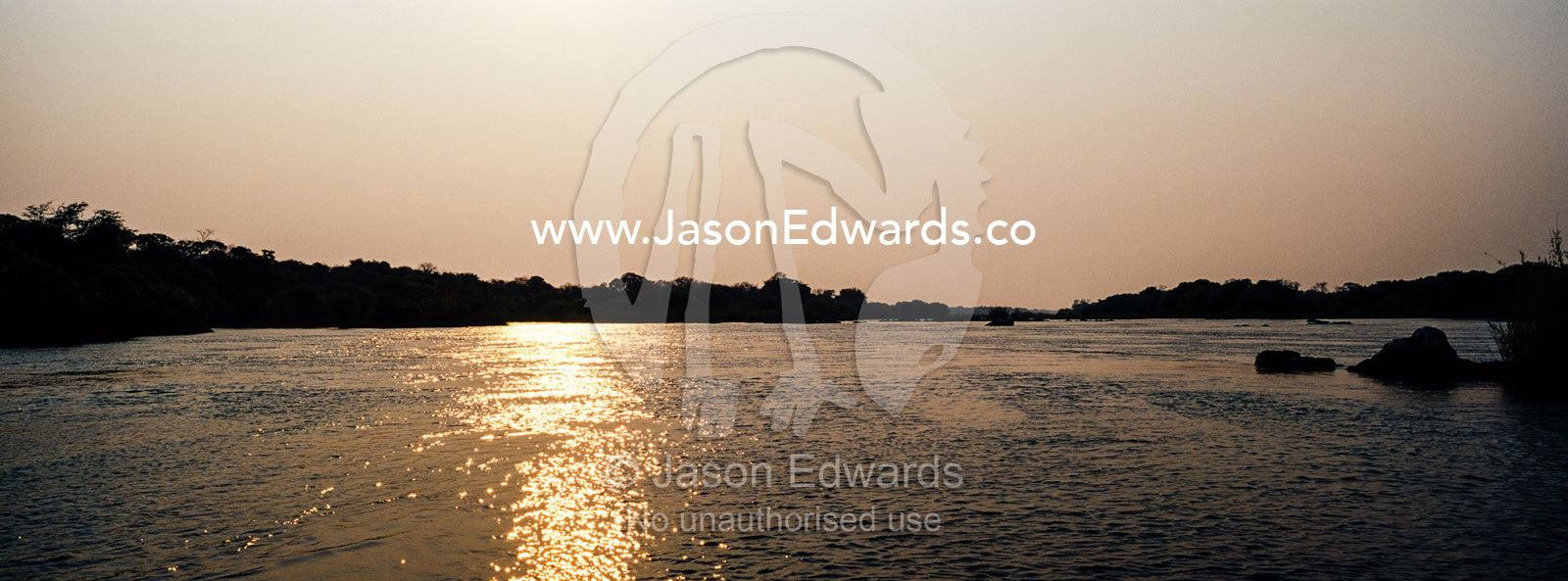 Dawn rises over a wide river flowing between riverbanks covered in forest. Chobe River, Chobe National Park, Botswana.