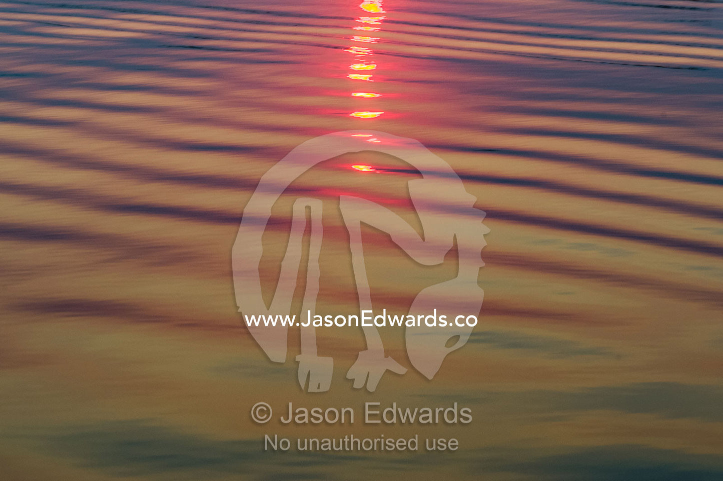 The red glow of sunset reflected in the calm surface and ripples of a wetland. Chobe River, Chobe National Park, Botswana.