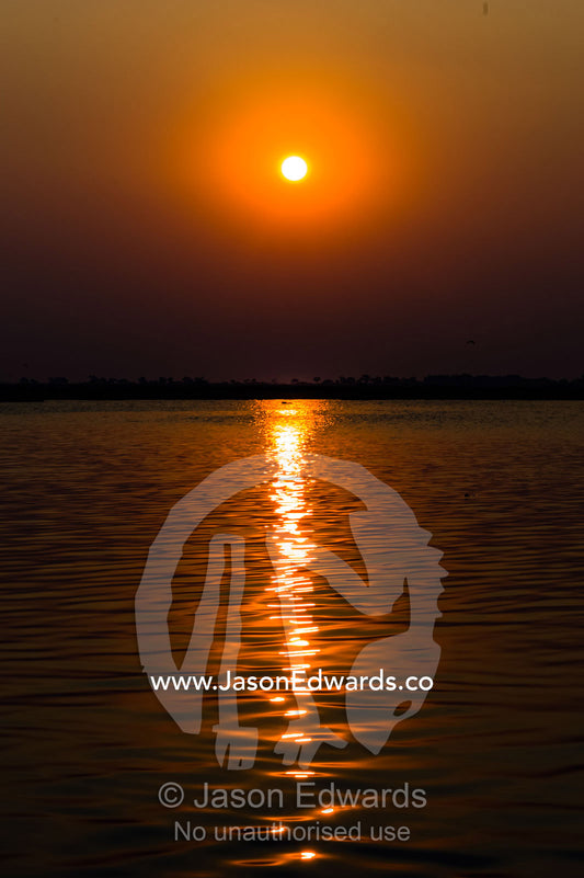A bright orange sunset reflected in the calm surface of a wetland. Chobe River, Chobe National Park, Botswana.