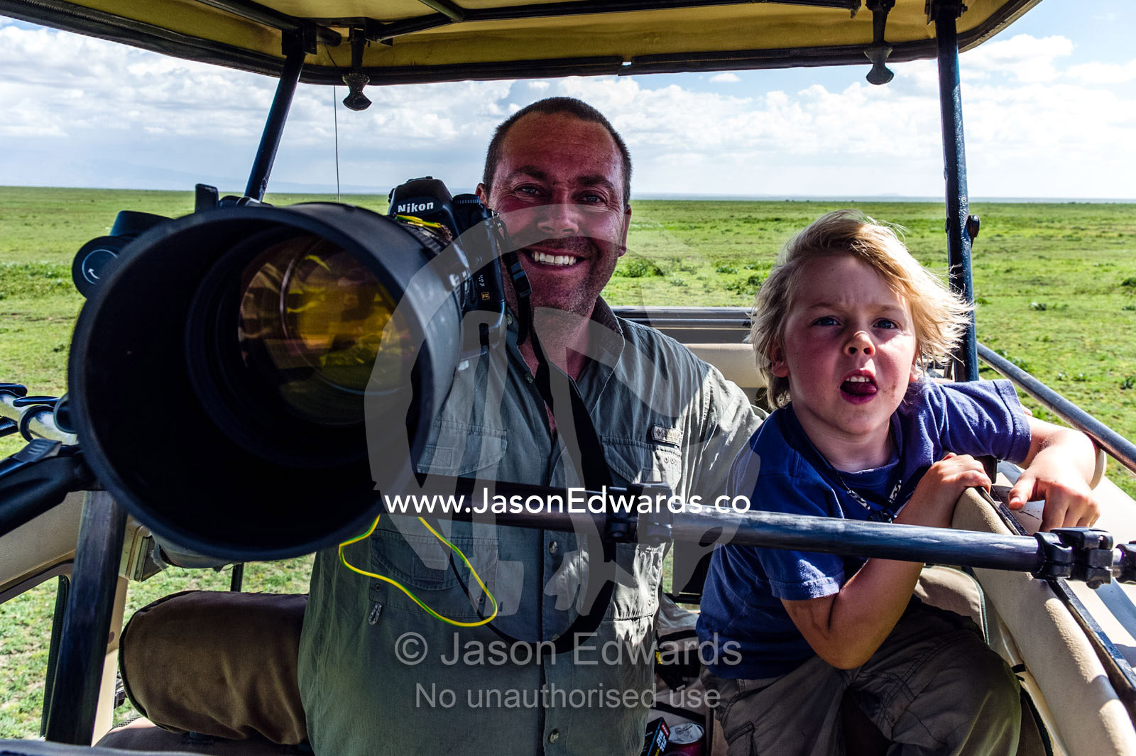 A wildlife photographer and his son with their camera on safari on the savannah. Ngorongoro Conservation Area, Ngorongoro District, Tanzania, Africa.