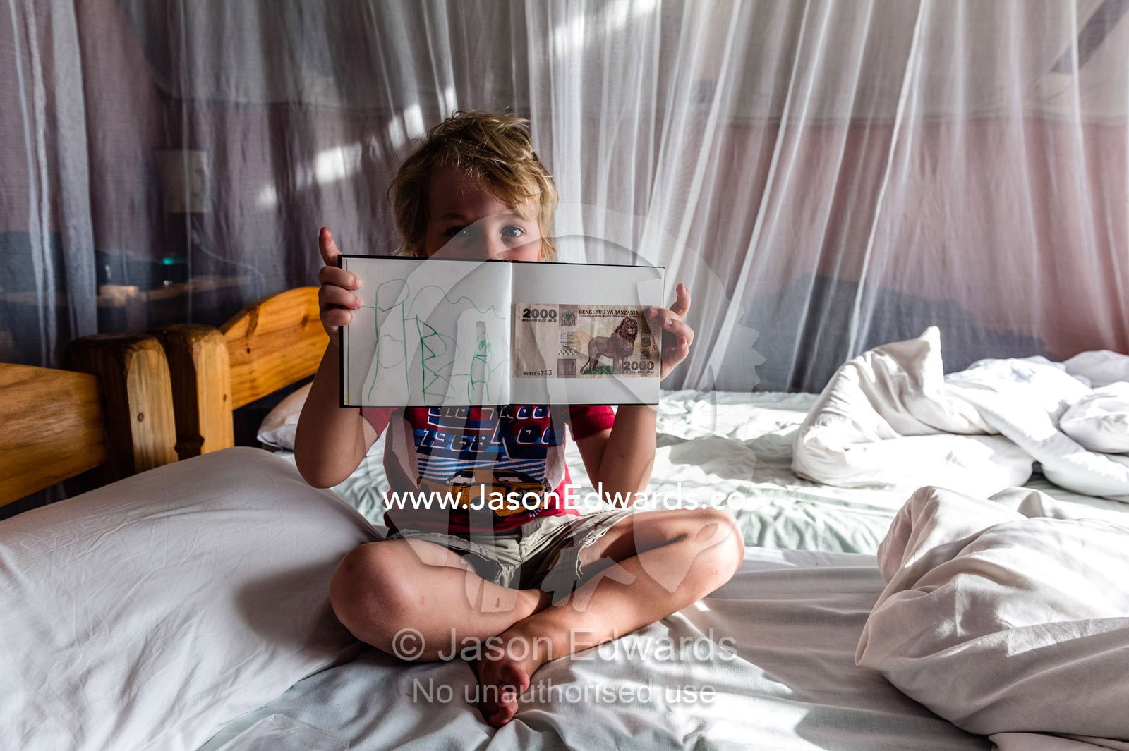 A small boy proudly displays his African safari journal drawing and money collection. Mto Wa Mbu, Lake Manyara National Park, Monduli District, Arusha Region, Tanzania, Africa.