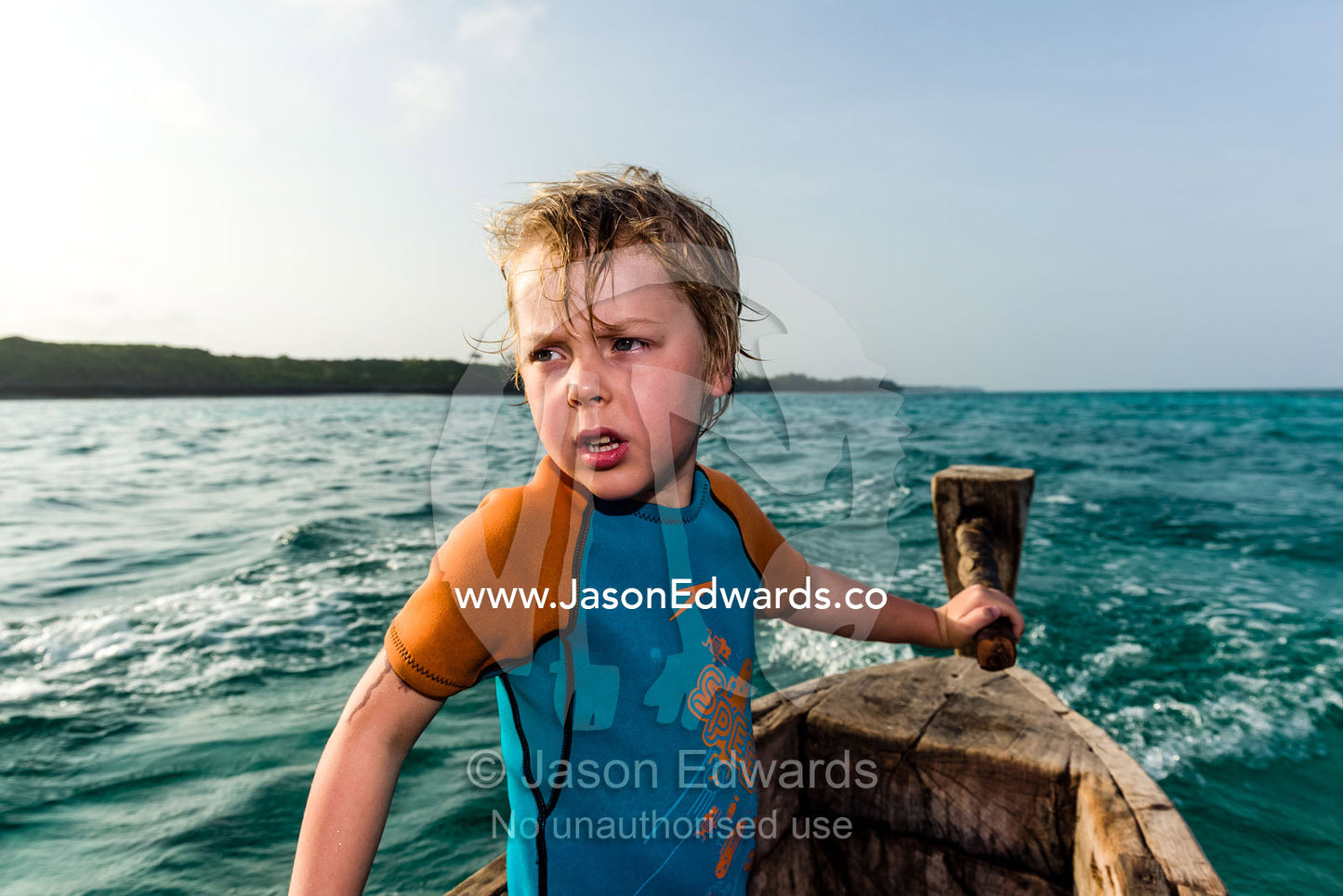 A small boy steers a wooden trimaran fishing dhow on the turquoise seas of the Indian Ocean. Bwejuu, Unguja Island, Zanzibar, Tanzania, Africa.