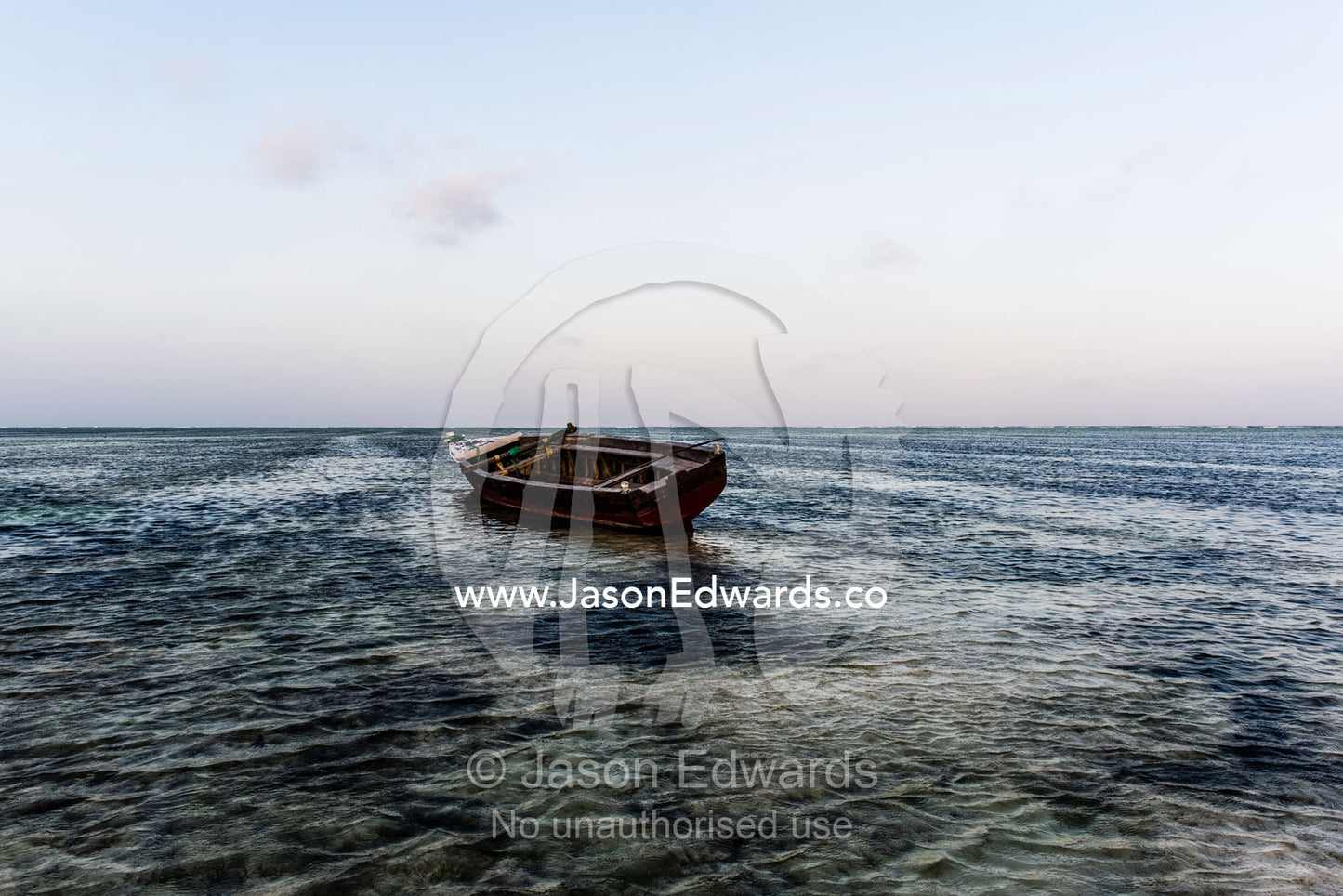 A fishing boat moored in the shallows of a tropical island in the Indian Ocean. Bwejuu, Echo Beach Hotel, Echo Beach, Unguja Island, Zanzibar, Tanzania, Africa.