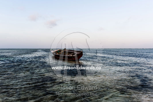 A fishing boat moored in the shallows of a tropical island in the Indian Ocean. Bwejuu, Echo Beach Hotel, Echo Beach, Unguja Island, Zanzibar, Tanzania, Africa.