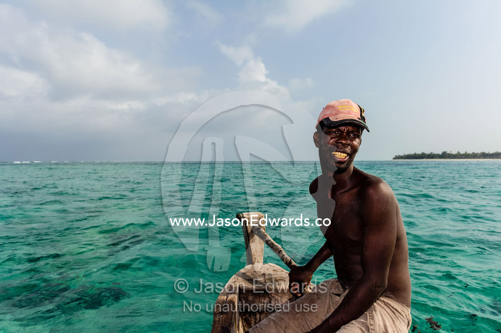 A fisherman steers his wooden trimaran sailing dhow in the shallow Indian Ocean. Bwejuu, Unguja Island, Zanzibar, Tanzania, Africa.